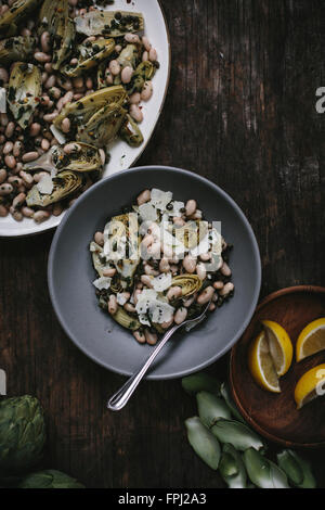 Un bol de salade d'artichaut bébé braisé aux haricots blancs et manchego rasée est photographié par le haut. Banque D'Images