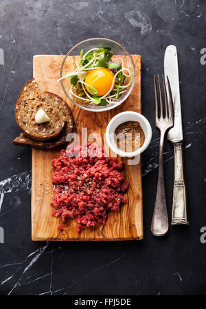 Steak tartare de boeuf avec salade et toasts à l'ail sur fond de marbre noir Banque D'Images