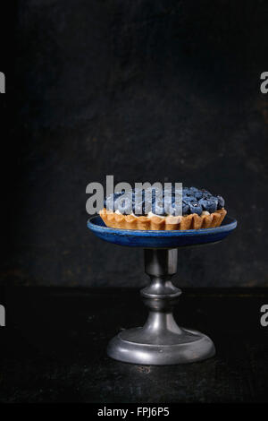 Tartelette au citron avec des bleuets frais, servis sur vintage cake stand sur fond noir. Banque D'Images