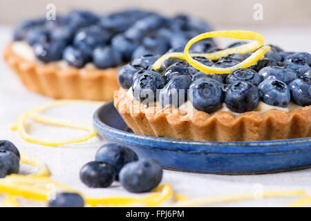 Close up de deux tartelettes au citron avec des bleuets frais, servis sur une plaque en céramique bleu blanc sur fond textile. Banque D'Images