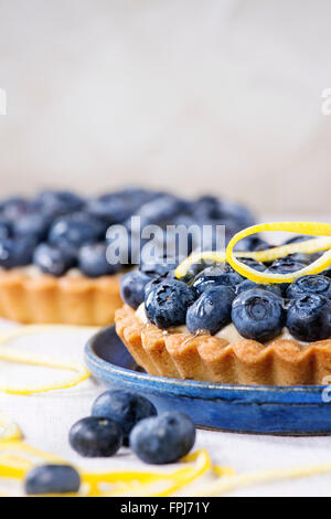 Close up de deux tartelettes au citron avec des bleuets frais, servis sur une plaque en céramique bleu blanc sur fond textile. Banque D'Images