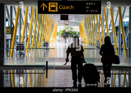 Vue arrière de deux voyageurs en silhouettes marchent vers une baie de transport d'autocar dans le hall d'arrivée T3 de l'aéroport Changi de Singapour. SG Banque D'Images