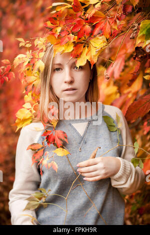 Autumn girl portrait en rouge jaune feuilles de lierre en orientation verticale, jeune fille aux cheveux blonds en chandail gris, l'automne nature Banque D'Images