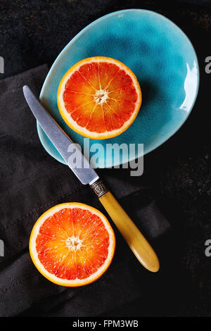 Tranches de fruits orange sanguine de Sicile sur les plaques en céramique turquoise brillant sur fond noir, avec couteau et napk textiles vintage Banque D'Images