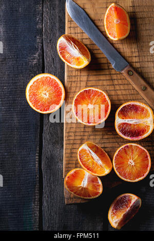 Tranches de fruits oranges sanguines de Sicile sur planche en bois sombre sur fond de bois. Vintage avec couteau. Vue d'en haut Banque D'Images