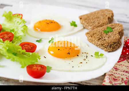 Le petit-déjeuner sur la Saint-Valentin - œufs au plat et du pain en forme de cœur et des légumes frais. Banque D'Images