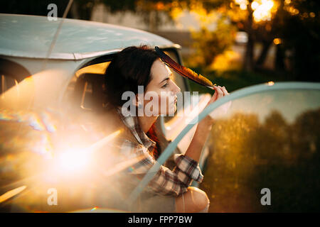 Femme assise avec plume dans la voiture, à la recherche dans la distance Banque D'Images