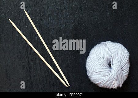 Pelote de fil blanc avec des aiguilles à tricoter en bambou avec fond en ardoise noire Banque D'Images