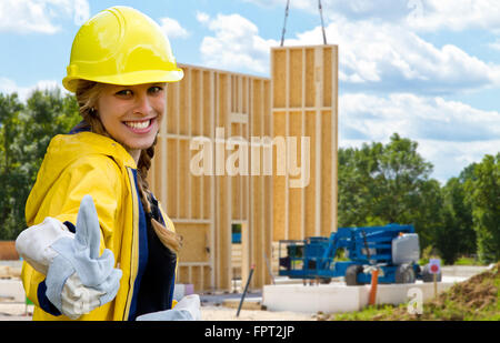 Jeune femme sur un chantier avec pouce vers le haut. Dans un contexte de bâtiments préfabriqués en bois Banque D'Images