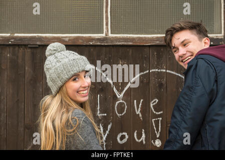 Jeune couple debout près de mur sur lequel est appelée coeur et l'amour vous écrit sur un mur en bois, Munich, Bavière, Allemagne Banque D'Images