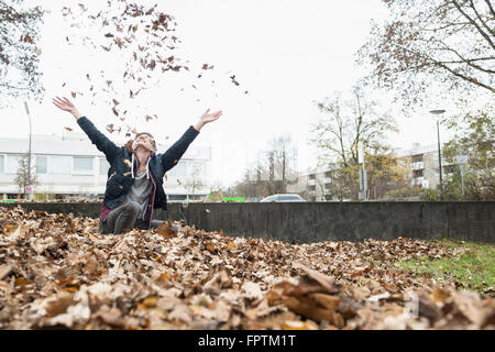 Jeune homme jetant des feuilles sèches de l'automne dans l'air, Munich, Bavière, Allemagne Banque D'Images