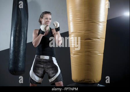 Jeune femme faisant la formation de force en enfonçant le sac dans la salle de sport, Bavière, Allemagne Banque D'Images