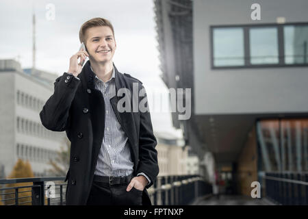 Homme d'attendre que quelqu'un d'adolescent et talking on cellphone et souriant, Bavière, Allemagne Banque D'Images