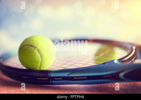 Balle de tennis reposant sur une raquette de tennis sur un cour d'asphalte rouge Banque D'Images