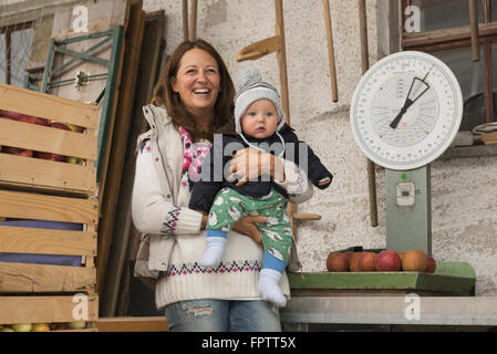 Agriculteur biologique femme avec son bébé debout dans l'échelle de la ferme et à l'arrière-plan, Bavière, Allemagne Banque D'Images