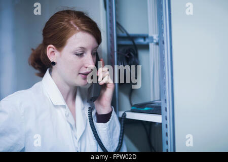 Jeune ingénieur femelle en conversation sur téléphone fixe dans la salle de commande, Freiburg im Breisgau, Bade-Wurtemberg, Allemagne Banque D'Images