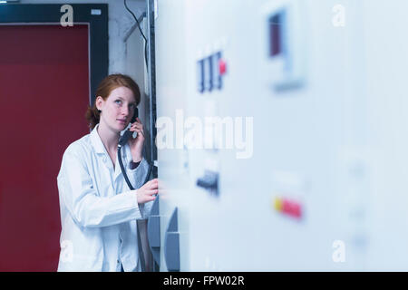 Jeune ingénieur femelle en conversation sur téléphone fixe dans la salle de commande, Freiburg im Breisgau, Bade-Wurtemberg, Allemagne Banque D'Images