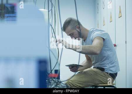 Ingénieur mâle holding digital tablet et la réparation d'un appareil en laboratoire, Freiburg im Breisgau, Bade-Wurtemberg, Allemagne Banque D'Images