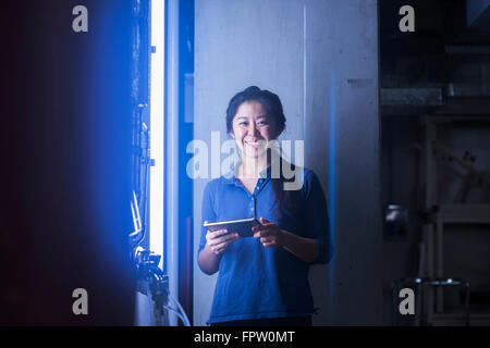 Jeune ingénieur femelle using digital tablet et souriant dans une installation industrielle, Freiburg im Breisgau, Bade-Wurtemberg, Allemagne Banque D'Images