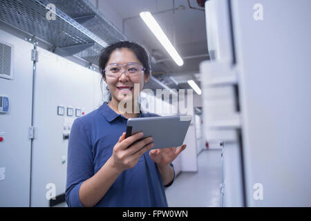 Jeune ingénieur femelle panneau de mise à jour par tablette numérique dans une industrie, Freiburg im Breisgau, Bade-Wurtemberg, Allemagne Banque D'Images