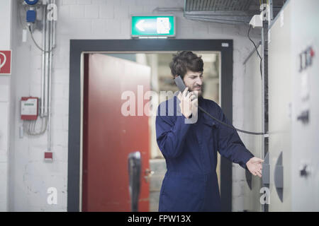 Ingénieur jeune mâle en conversation sur téléphone fixe dans une installation industrielle, Freiburg im Breisgau, Bade-Wurtemberg, Allemagne Banque D'Images