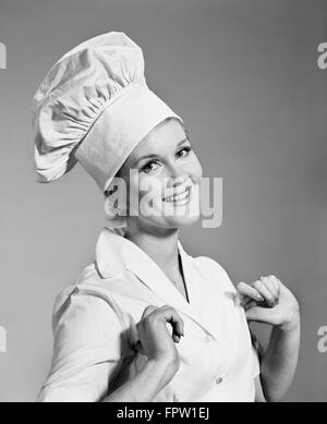 1960 SMILING WOMAN WEARING FIERS CHEFS HAT TOQUE DU CHEF LOOKING AT CAMERA Banque D'Images