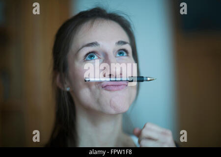 Young woman holding pen entre le nez et les lèvres, Freiburg im Breisgau, Bade-Wurtemberg, Allemagne Banque D'Images