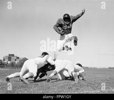 1960 JOUEUR DE FOOTBALL sautant par-dessus les joueurs bloqués Banque D'Images