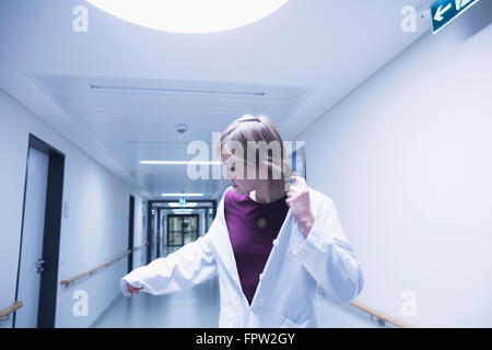 Jeune femme médecin regardant sa main tout en marchant dans le couloir de l'hôpital, Freiburg im Breisgau, Bade-Wurtemberg, Allemagne Banque D'Images