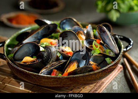 Style asiatique délicieuses moules vapeur avec le poivron rouge, oignon vert, coriandre et noix de coco dans un bouillon. Banque D'Images