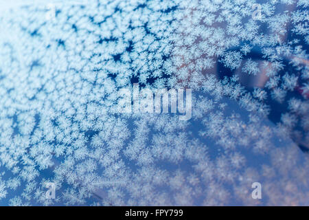 Frost modes sur une fenêtre en verre crée des motifs d'hiver bleu avec un fond de ciel d'hiver. Banque D'Images