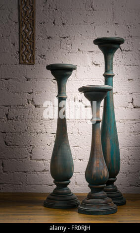 Composition de trois chandeliers en bois vintage gris bleu sur fond de parquet au sol et mur de briques peintes en blanc Banque D'Images