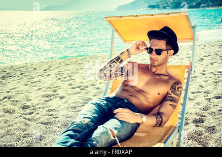 Young handsome man on beach portant sur un transat et de repos de la capture d'un tan. Arrière-plan sur la mer Banque D'Images