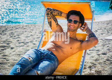 Young handsome man on beach portant sur transat profitant de la place, souriant à la caméra. Sur fond de paysage marin Banque D'Images