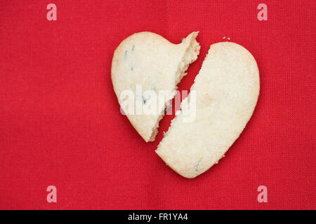 A broken heart shaped biscuit sur un fond rouge. Banque D'Images