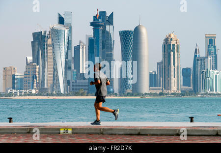 Mann le jogging sur front de mer Corniche en direction de tours de bureaux modernes à West Bay, quartier financier et d'affaires à Doha Qatar Banque D'Images