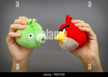 Tambov, Fédération de Russie - Mars 03, 2016 Angry Bird rouge et Bad Piggy jouets mous en personne les mains sur fond gris. Banque D'Images
