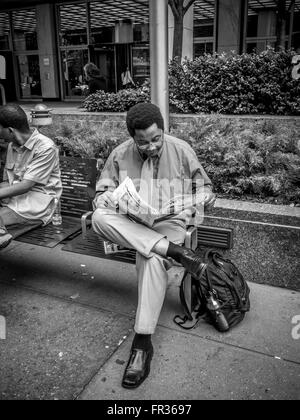 Businessman assis sur un banc à l'extérieur la lecture de journal, New York City, USA. Banque D'Images