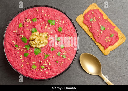 L'hummus de betteraves dans un bol noir, une coupe d'or et une tranche de pain avec de l'houmous de betterave sur une plaque en ardoise Banque D'Images