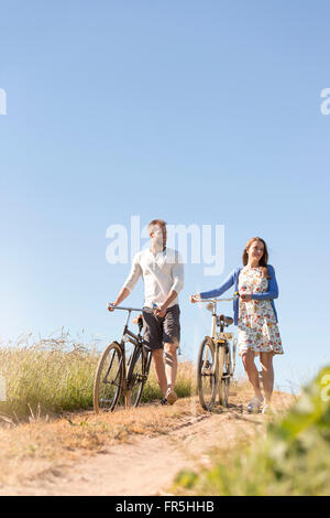 Jeune couple en train de marcher des vélos sur route de terre ci-dessous sunny blue sky Banque D'Images