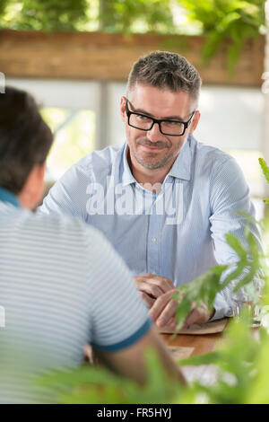 Smiling man listening to friend au cafe table Banque D'Images