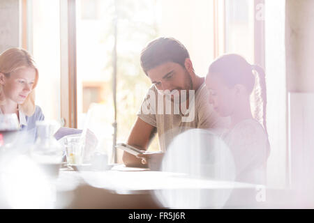 Père et fille using digital tablet in sunny cafe Banque D'Images