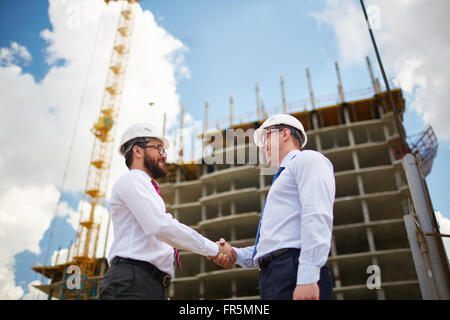 Deux jeunes architectes au casque de chaque message d'autres avec handshake Banque D'Images