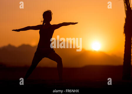 Silhouette de jeune femme pratiquant le yoga ou Pilates au coucher et au lever du soleil dans un magnifique endroit en montagne, faire une fente de l'exercice, Banque D'Images