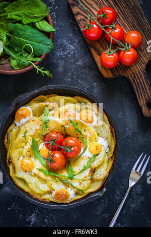 Frittata aux pommes de terre déjeuner aux épinards, tomates cerises et fromage dans la poêle. Vue de dessus de table sur fond noir. Still Life Banque D'Images