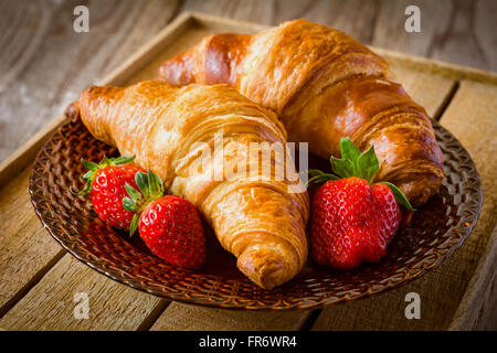 Des croissants frais avec des fraises sur la plaque sur fond de bois. Petit-déjeuner continental, un son chaud de l'alimentation Banque D'Images