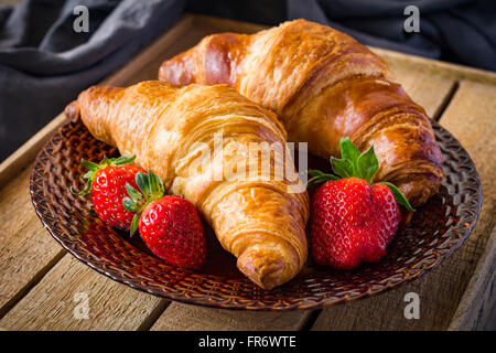 Des croissants frais avec des fraises sur la plaque sur fond de bois. Petit-déjeuner continental, un son chaud de l'alimentation Banque D'Images