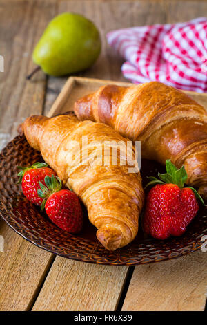 Des croissants frais avec des fraises sur la plaque sur fond de bois. Petit-déjeuner continental, un son chaud de l'alimentation Banque D'Images