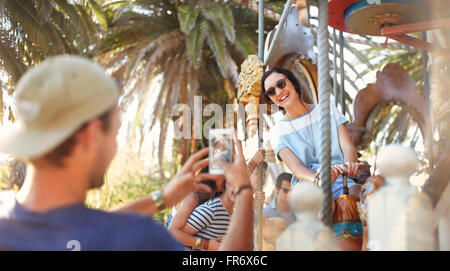 Young man photographing woman sur carousel au amusement park Banque D'Images