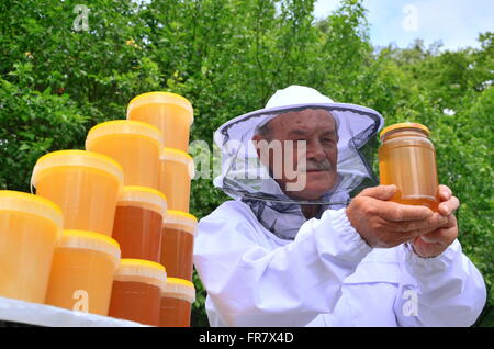 Apiculteur Senior présentant pot de miel frais dans le rucher dans le printemps Banque D'Images